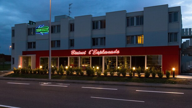 Un hôtel à la façade rouge et blanche, avec une enseigne lumineuse au néon et une entrée bien éclairée.