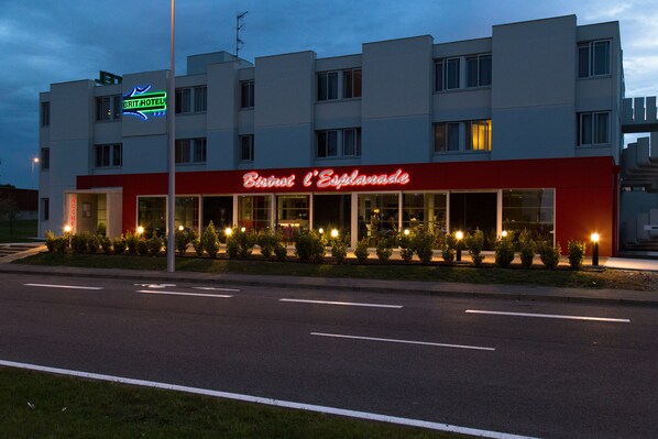 Un hotel con fachada roja y blanca, un letrero de neón y una entrada bien iluminada.