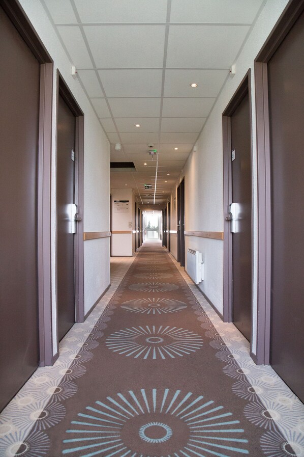 Passadís d'hotel amb una catifa estampada, portes a ambdós costats i un sostre amb il·luminació empotrada.