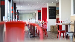 Een restaurantinterieur met rode en grijze stoelen, tafels en een menukaart op een prikbord.
