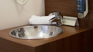 Un baño de hotel con lavamanos, espejo, secador de pelo y toallero.