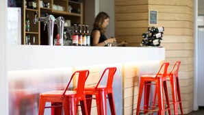 Een bar met rode barkrukken, een toonbank vol flessen en een persoon achter de bar.