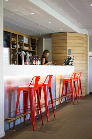Zona de bar con taburetes rojos, una barra con botellas y una persona sirviendo.