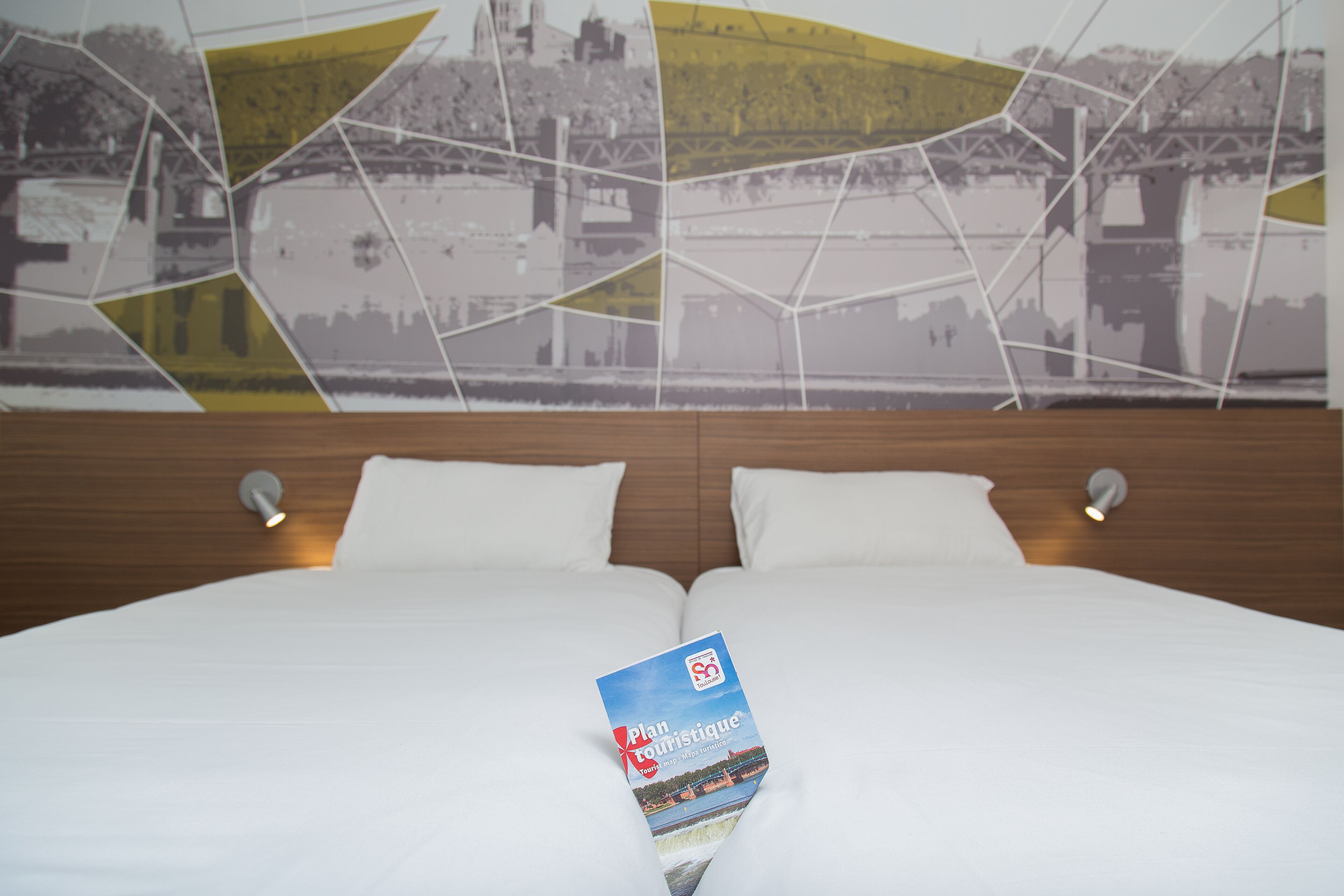 A hotel room with a bed, two pillows, and a brochure on the bed.