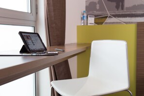 Un espacio de trabajo moderno con una tableta en un escritorio, una silla blanca y un panel amarillo.
