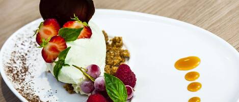 A dessert plate with a scoop of ice cream, strawberries, raspberries, and a chocolate piece on a white plate.