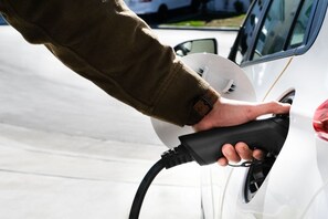 Una mano conectando un cable de carga al puerto de carga de un coche.