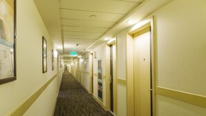 Un pasillo de hotel con puertas a la derecha, cuadros en la pared izquierda y suelo alfombrado.