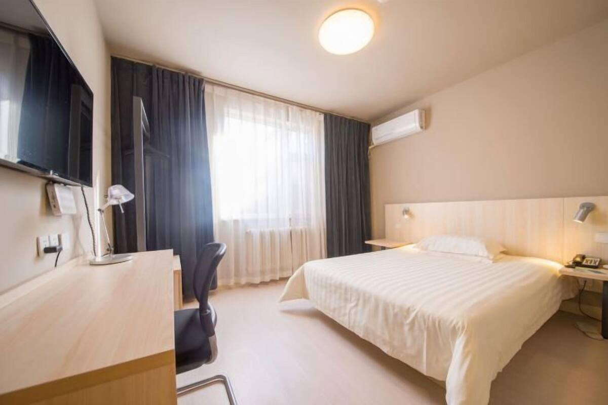 A hotel room with a bed, a desk, a chair, a TV, and a window with curtains.