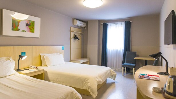 A hotel room with two beds, a desk, a chair, a small table, a wall-mounted air conditioner, a framed picture, and a window with curtains. - Jinjiang Inn (Jinan Daming Lake Baotu Spring) (Jinan)