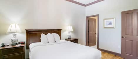 A hotel room with a large bed, two bedside tables with lamps, a wooden headboard, a door, and a framed picture on the wall.