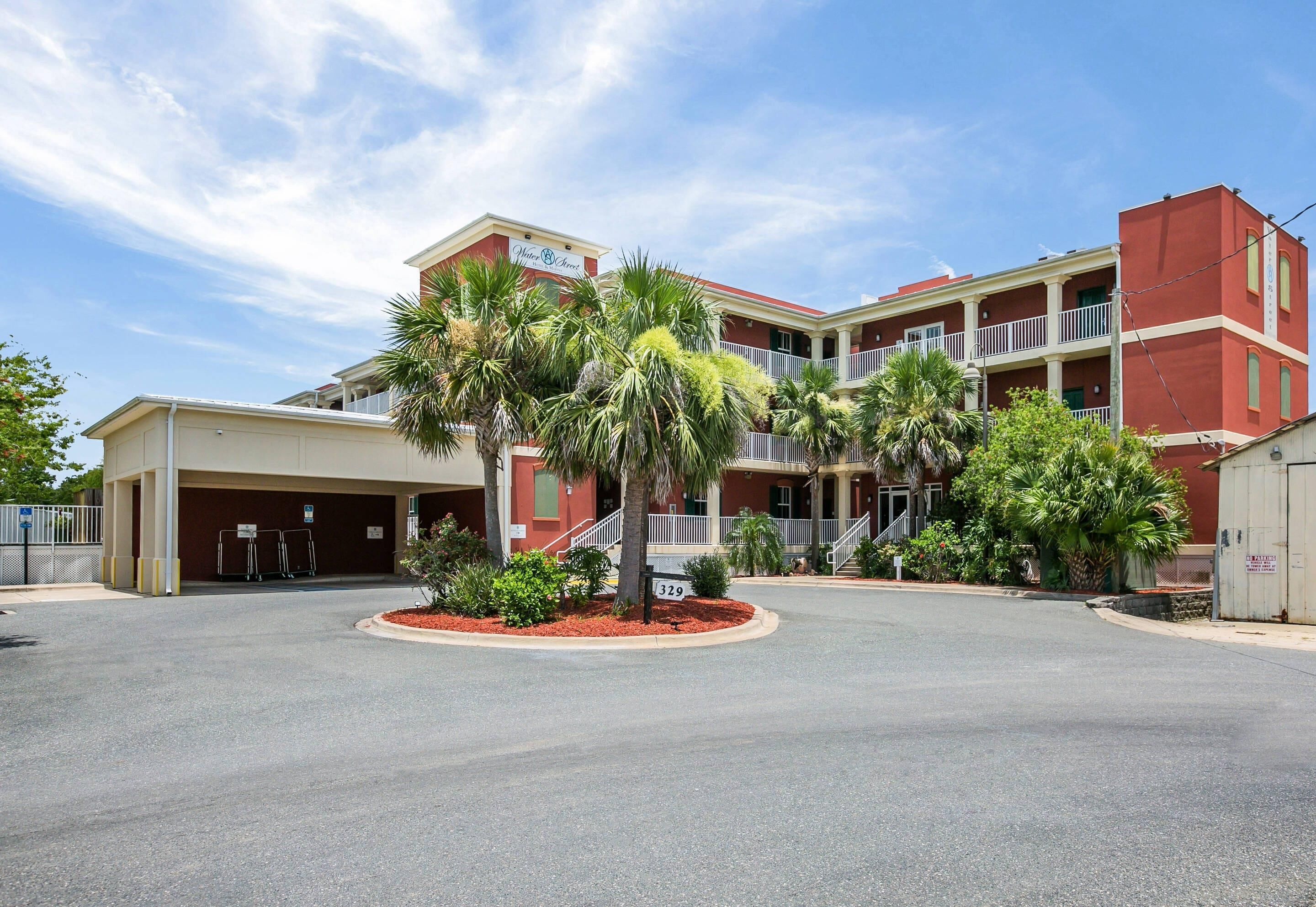 A hotel with a red facade, multiple balconies, and a parking area with palm trees.