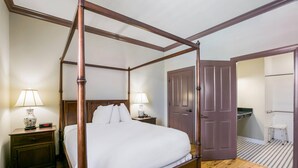 Una cama con dosel sobre un armazón de madera, dos mesitas de noche con lámparas, una puerta y un taburete pequeño.