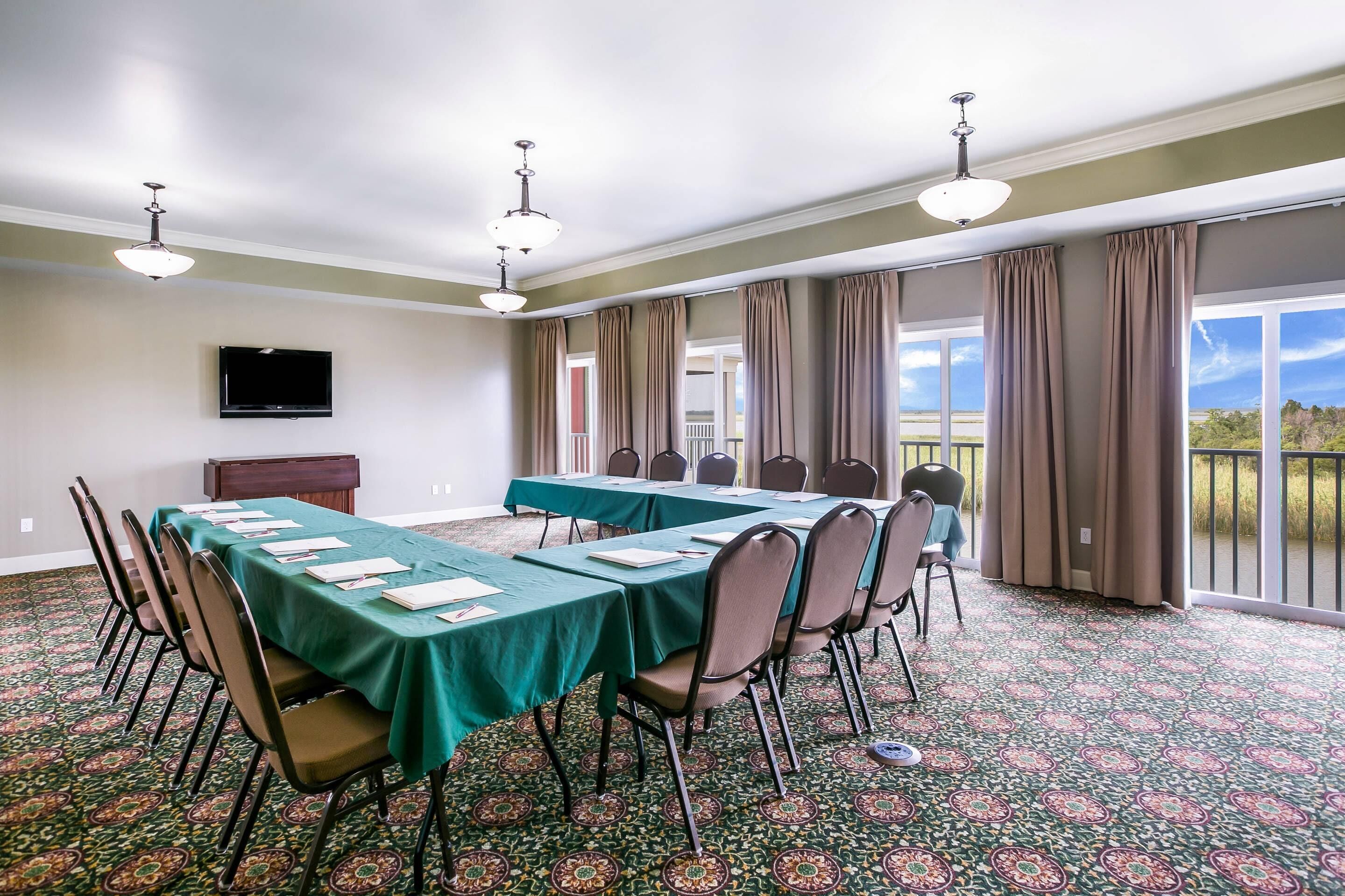 A conference room with a long table, chairs, a flat-screen TV, and large windows with curtains.
