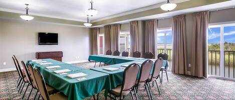 A conference room with a long table, chairs, a flat-screen TV, and large windows with curtains.
