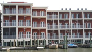 Un hotel de varios pisos con balcones, un muelle con barcos y vista al agua.