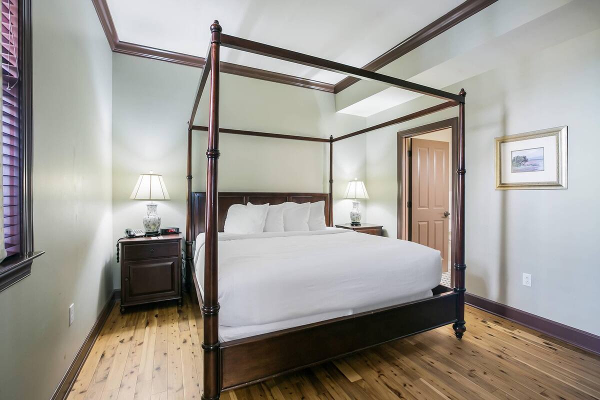 Un lit à baldaquin dans une pièce au plancher en bois, avec une porte visible au fond.