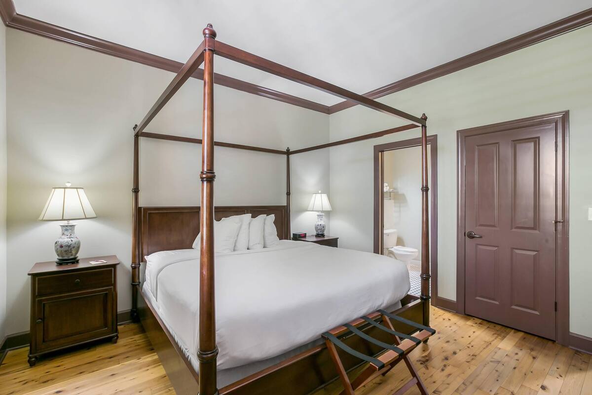 Un lit à baldaquin avec un cadre en bois, une table de chevet avec une lampe et une porte sur le côté droit.