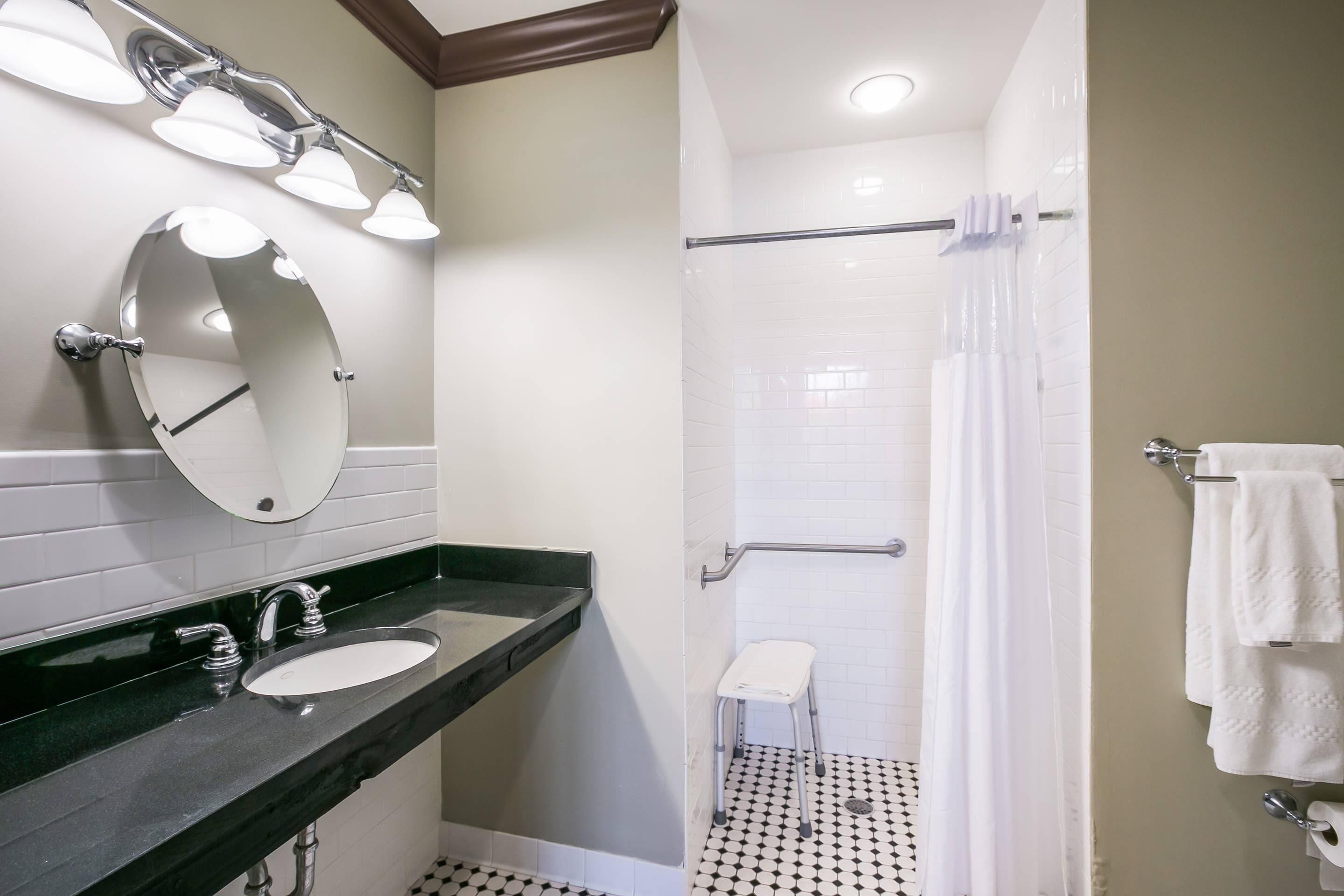 Une salle de bain avec un comptoir noir, deux lavabos, un miroir et une douche avec un rideau blanc.