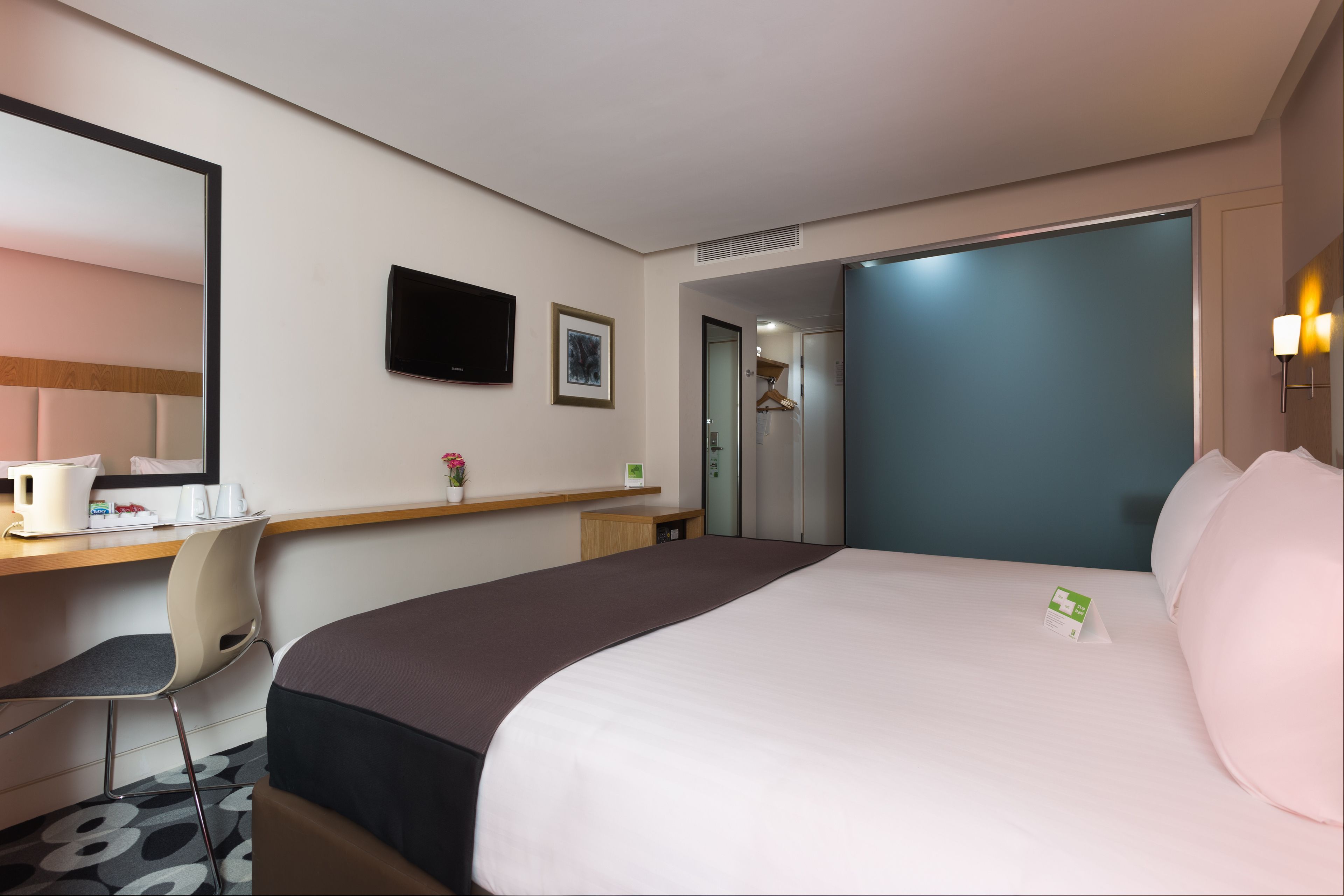 A hotel room with a bed, a desk with a chair, a TV, and a mirror.
