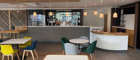 Zona de bar moderna con mostrador, taburetes y una variedad de botellas.