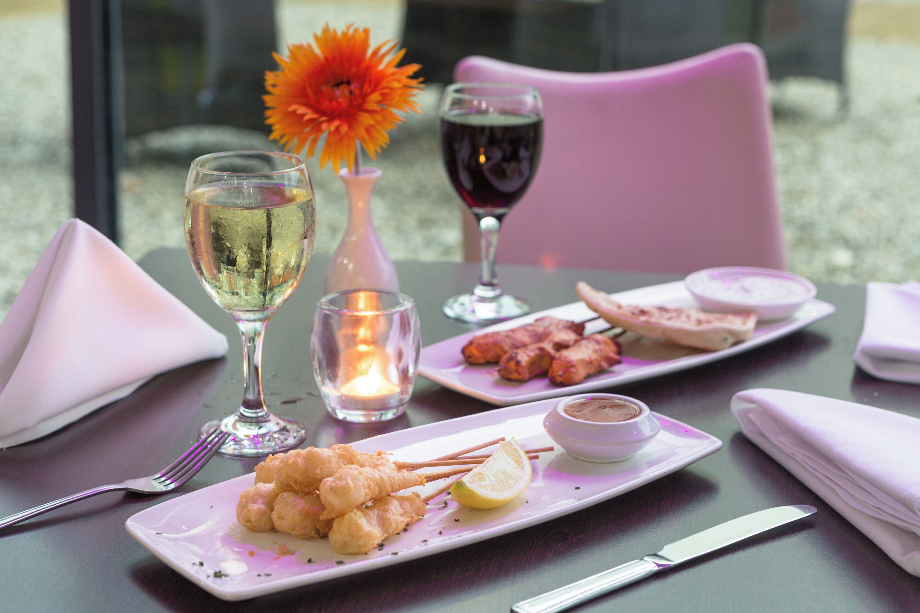 Une table dressée avec une assiette de fruits de mer frits, un verre de vin blanc, un verre de vin rouge, une bougie et une fleur.