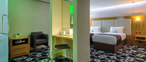 A hotel room with a bed, a desk, a chair, a small cabinet, and a patterned carpet.