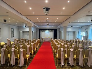 Een vergaderruimte met rijen gele stoelen en een rode gangpad, voorzien van plafondlampen en een podium aan de voorzijde.