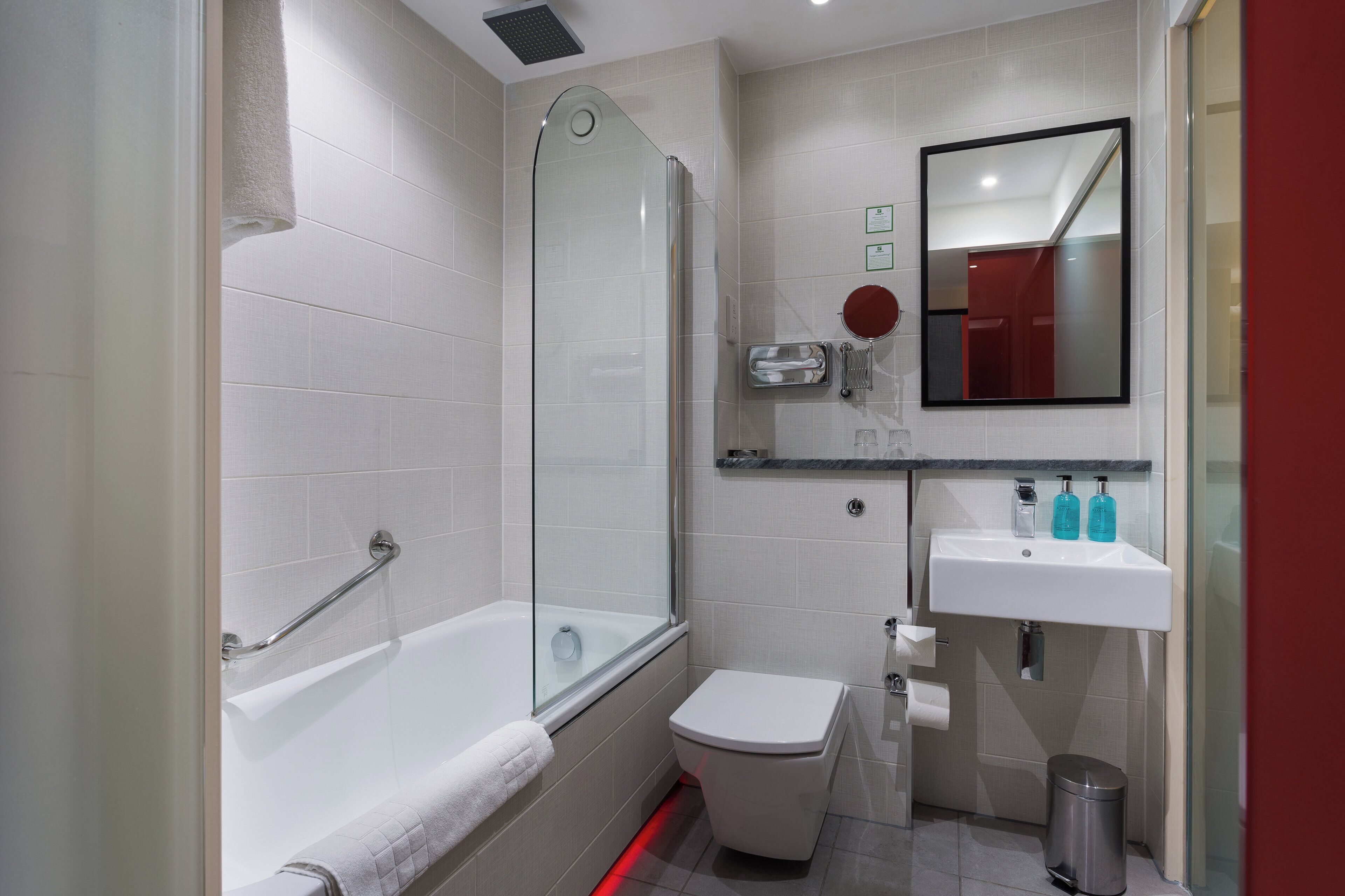 Ein modernes Badezimmer mit einer begehbaren Glasdusche, einer weißen Badewanne, einer Toilette und einem Waschbecken mit Spiegel.