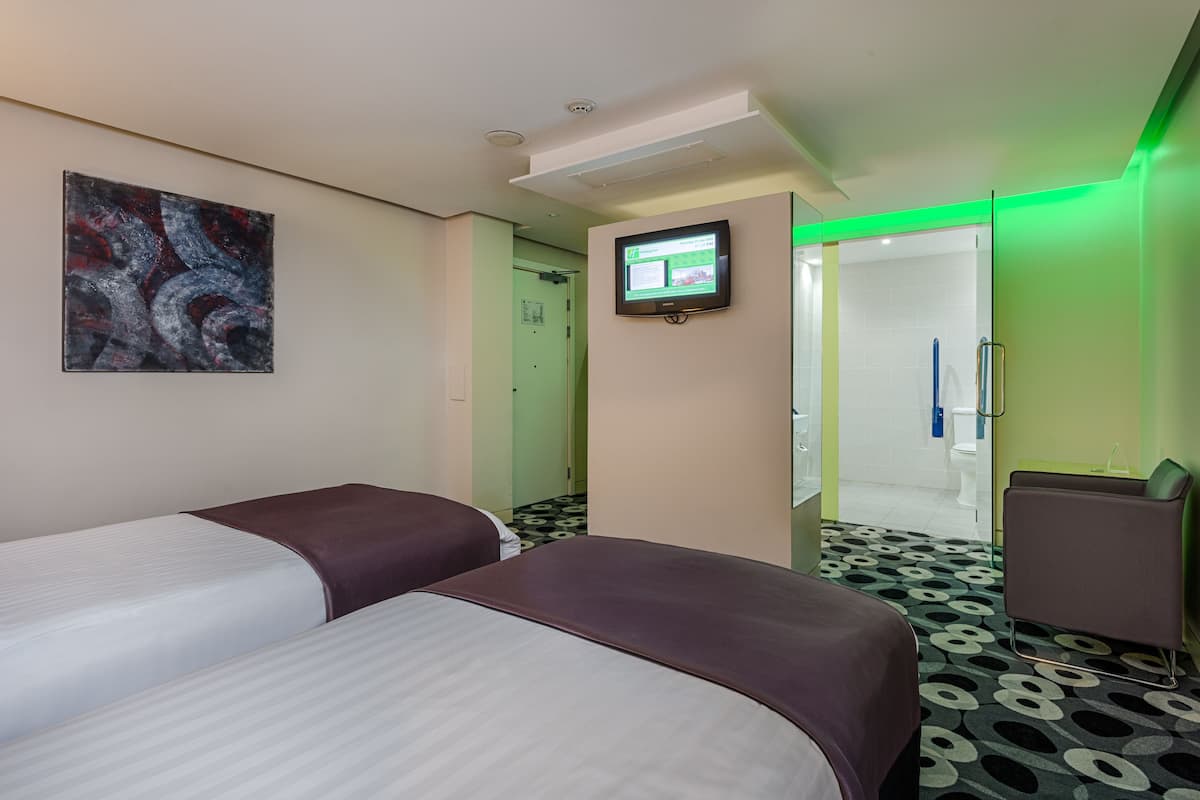 A hotel room with two beds, a TV, a green-lit mirror, and a patterned floor.