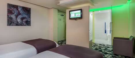 A hotel room with two beds, a TV, a green-lit mirror, and a patterned floor.