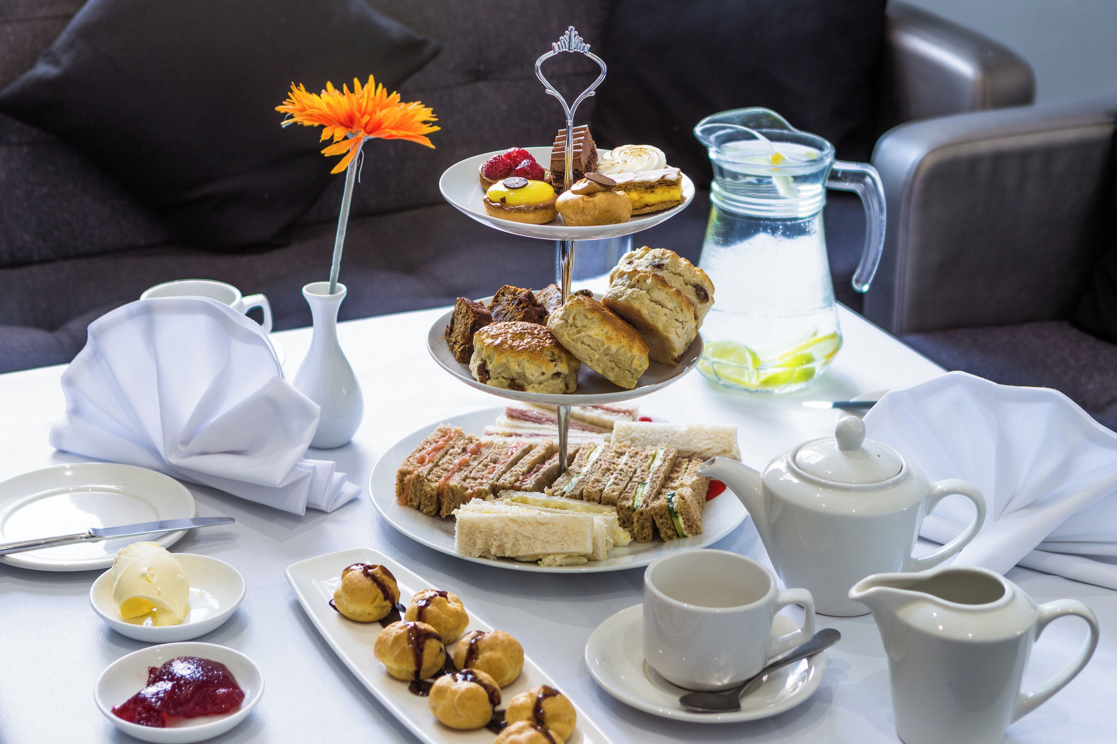 Una mesa dispuesta con un soporte escalonado para postres, sándwiches, scones y una tetera.