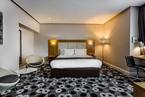 A hotel room with a large bed, a desk, a chair, and a small table with a vase of flowers.