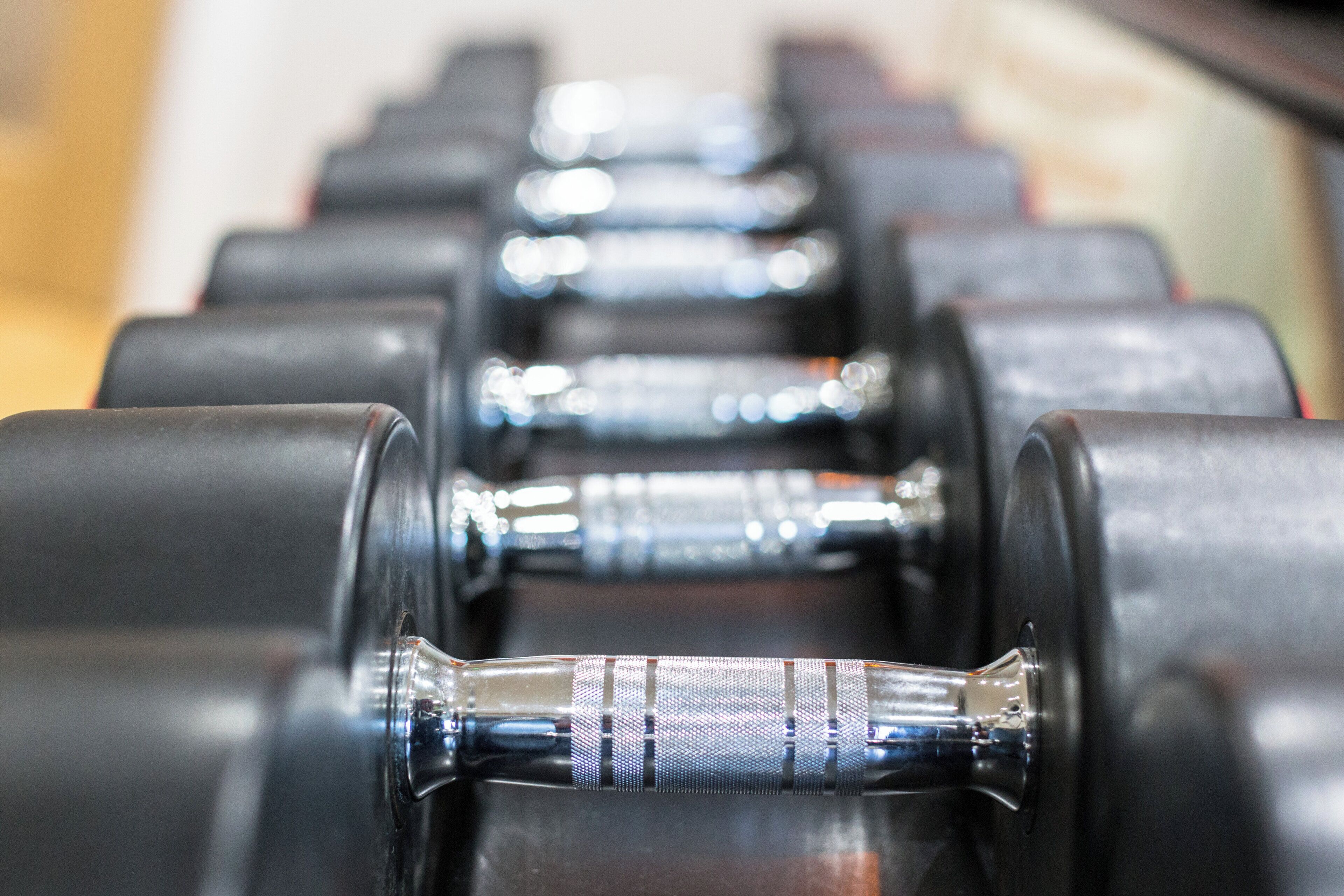 A row of black dumbbells with silver weights, arranged in a gym setting.