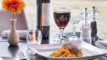 A dining table with a plate of food, wine glasses, a bottle of wine, and a vase with a flower.