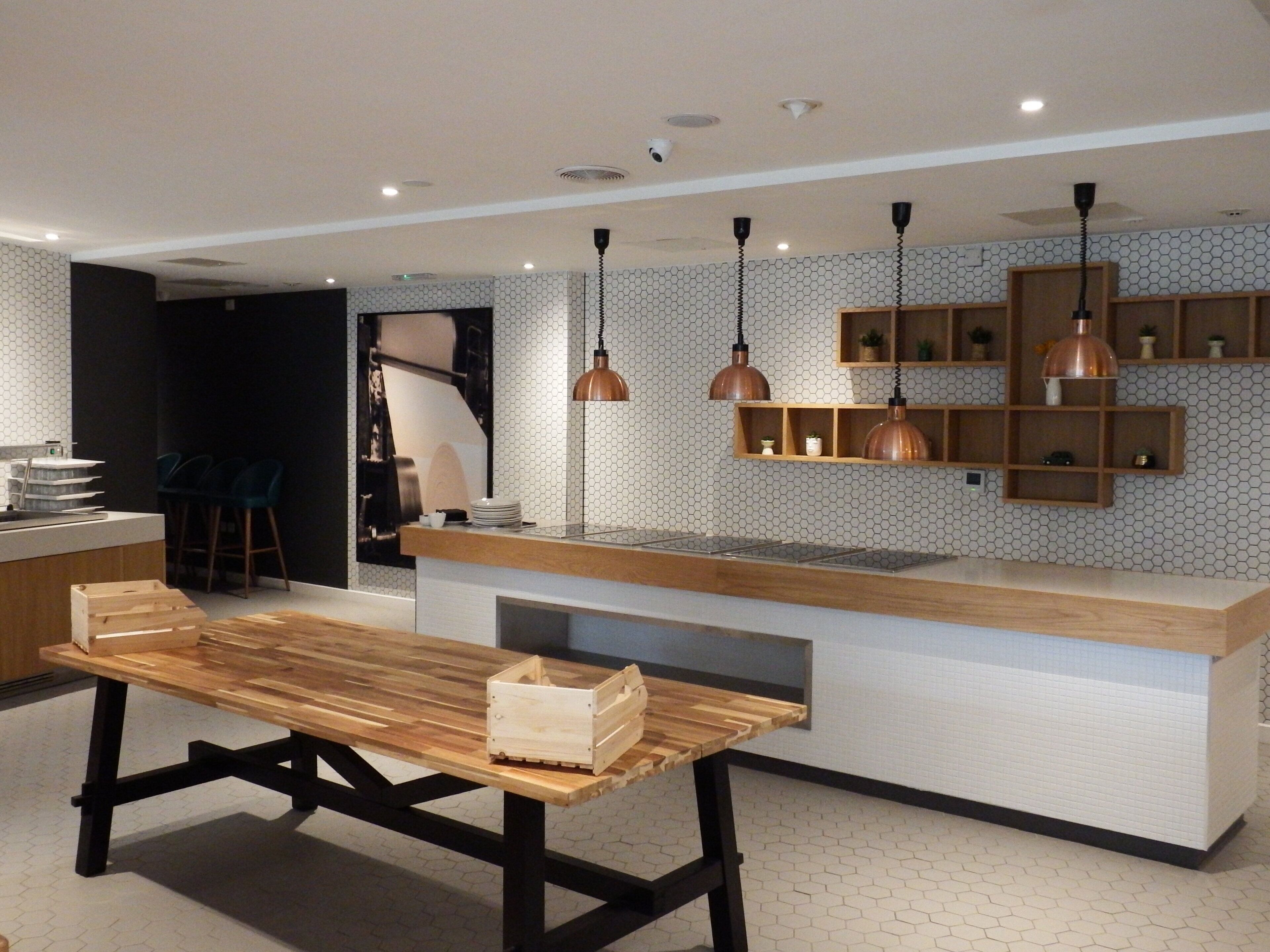 A modern kitchen with a wooden table, pendant lights, and a hexagonal patterned backsplash.