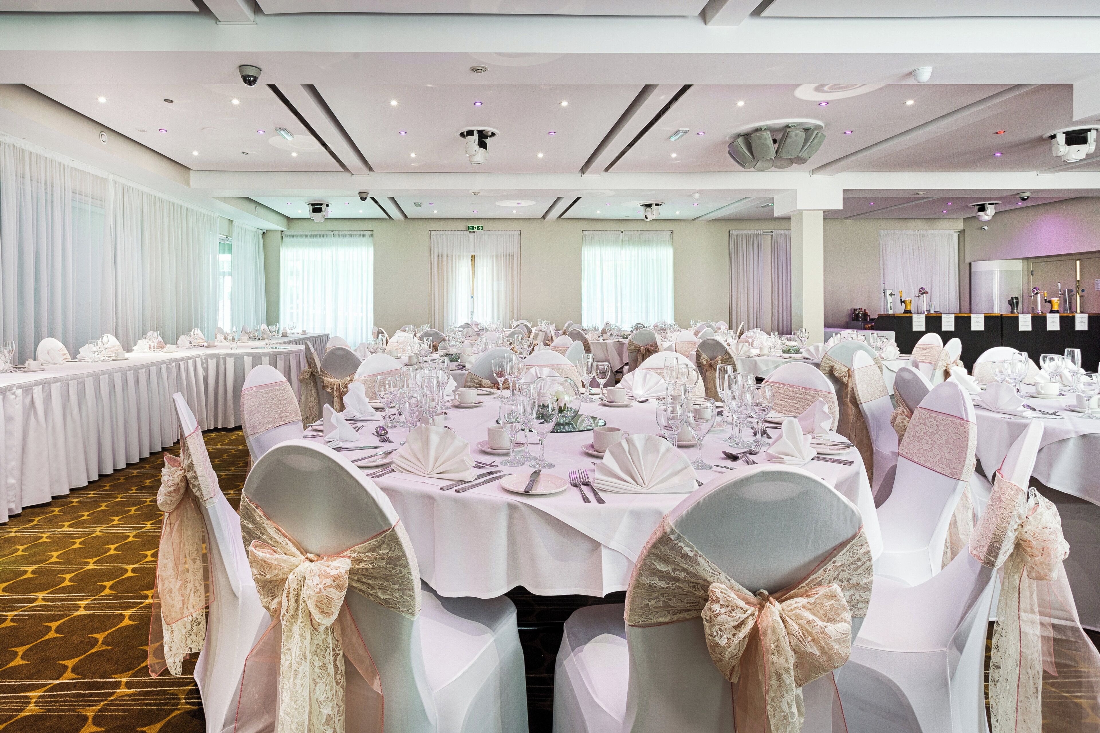 A banquet hall with round tables set for a formal event, featuring white tablecloths and chairs with bows.