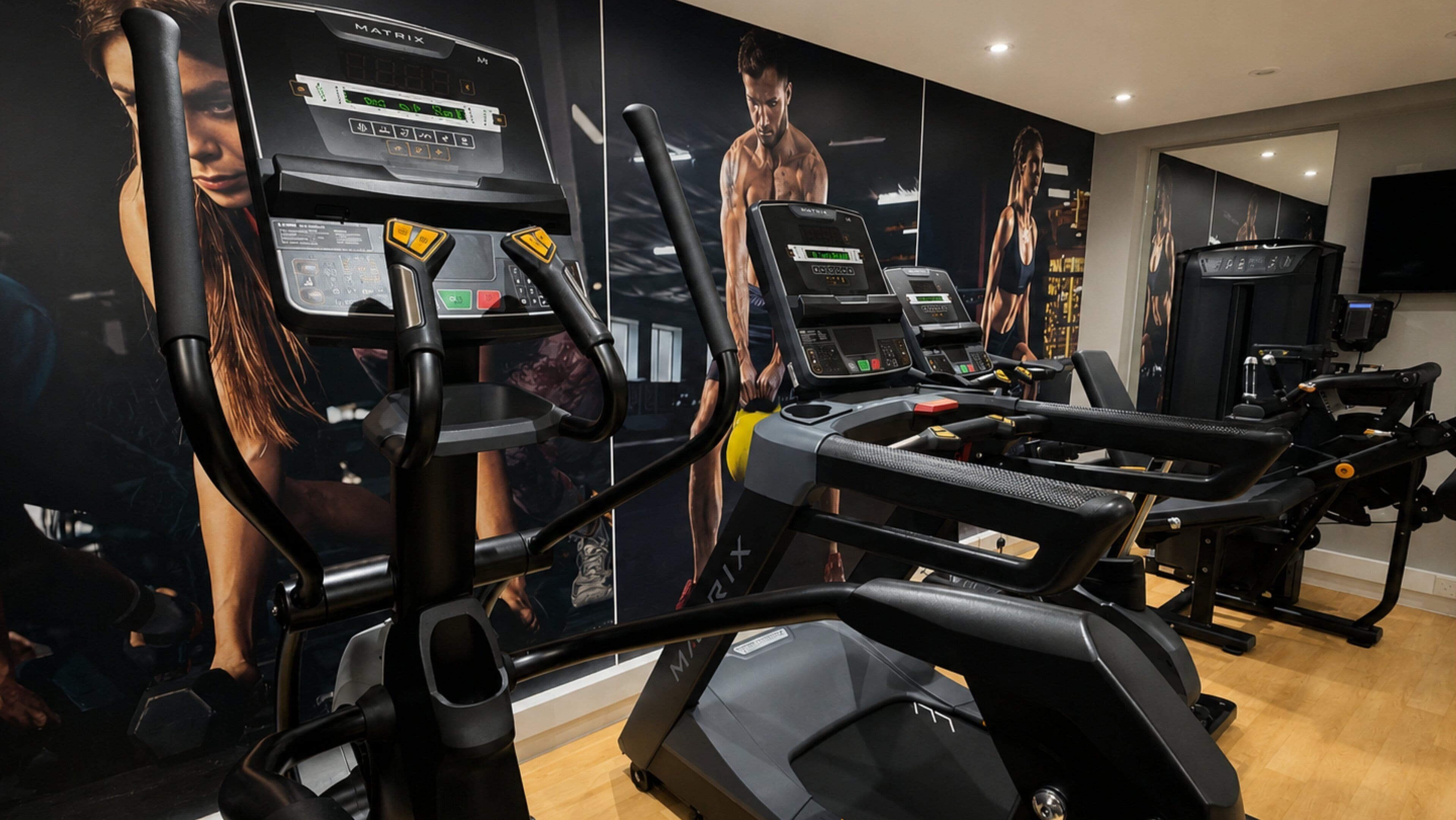 A gym with multiple treadmills, exercise bikes, and a mirrored wall with fitness posters.
