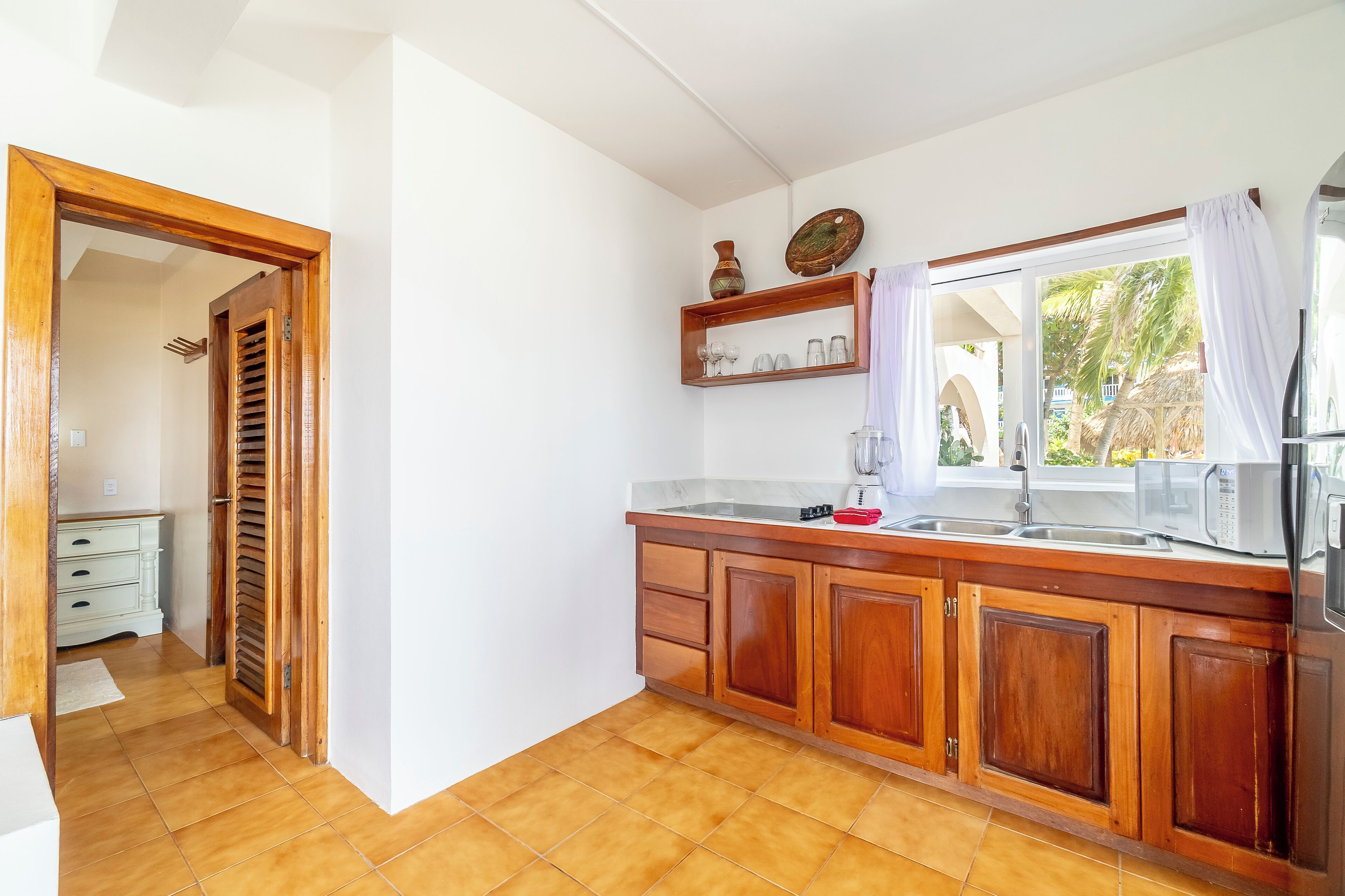 A kitchen with wooden cabinets, a countertop, a sink, and a window with curtains.