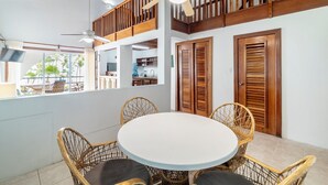 Un comedor con una mesa redonda, sillas de mimbre, un ventilador de techo y puertas de madera.