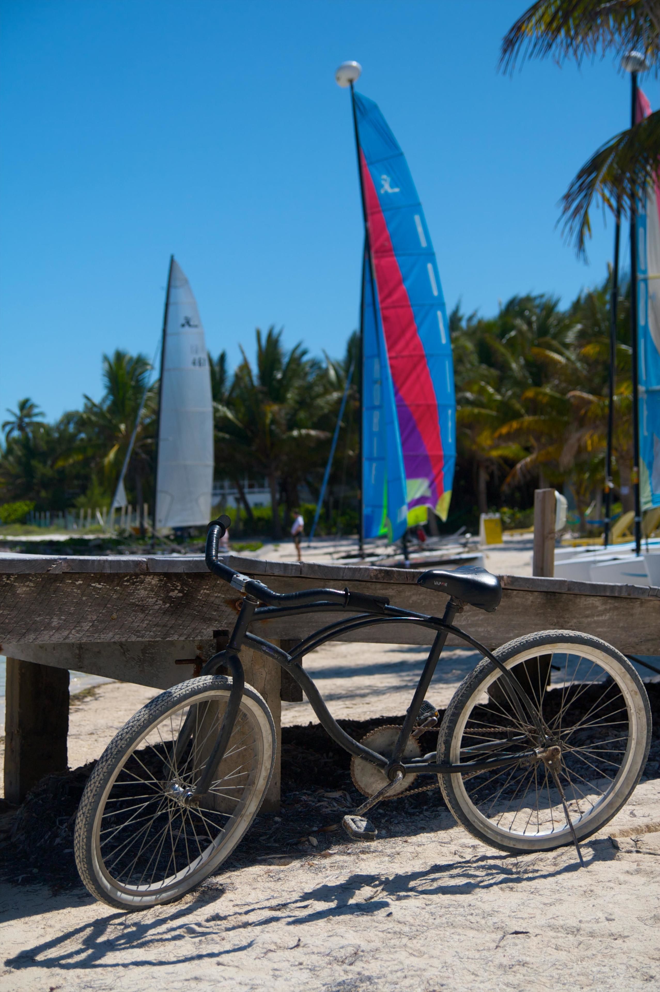 A bicycle parked on a sandy surface with a sailboat in the background.