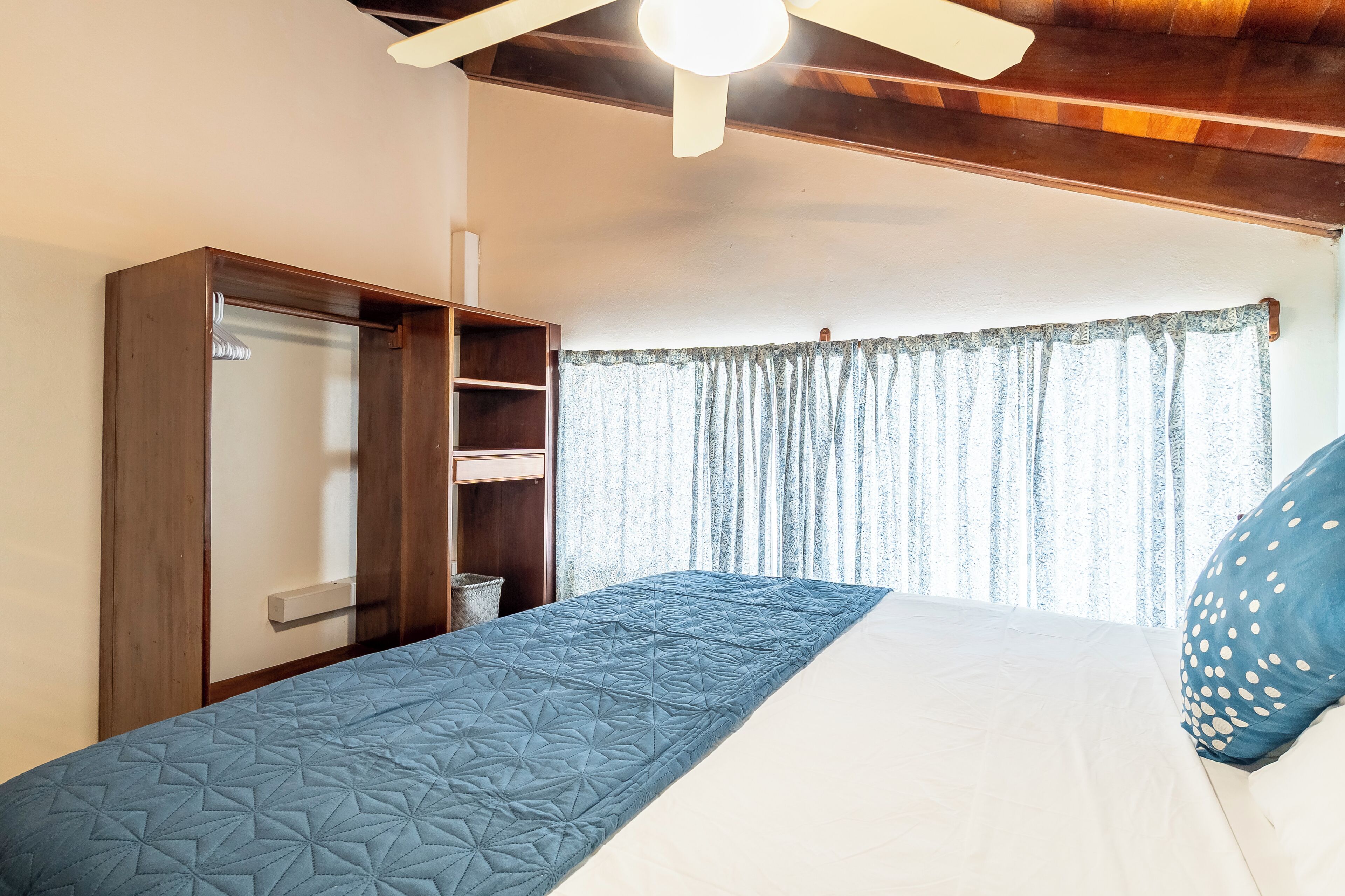 A bedroom with a bed, a wardrobe, a ceiling fan, and a window with curtains.