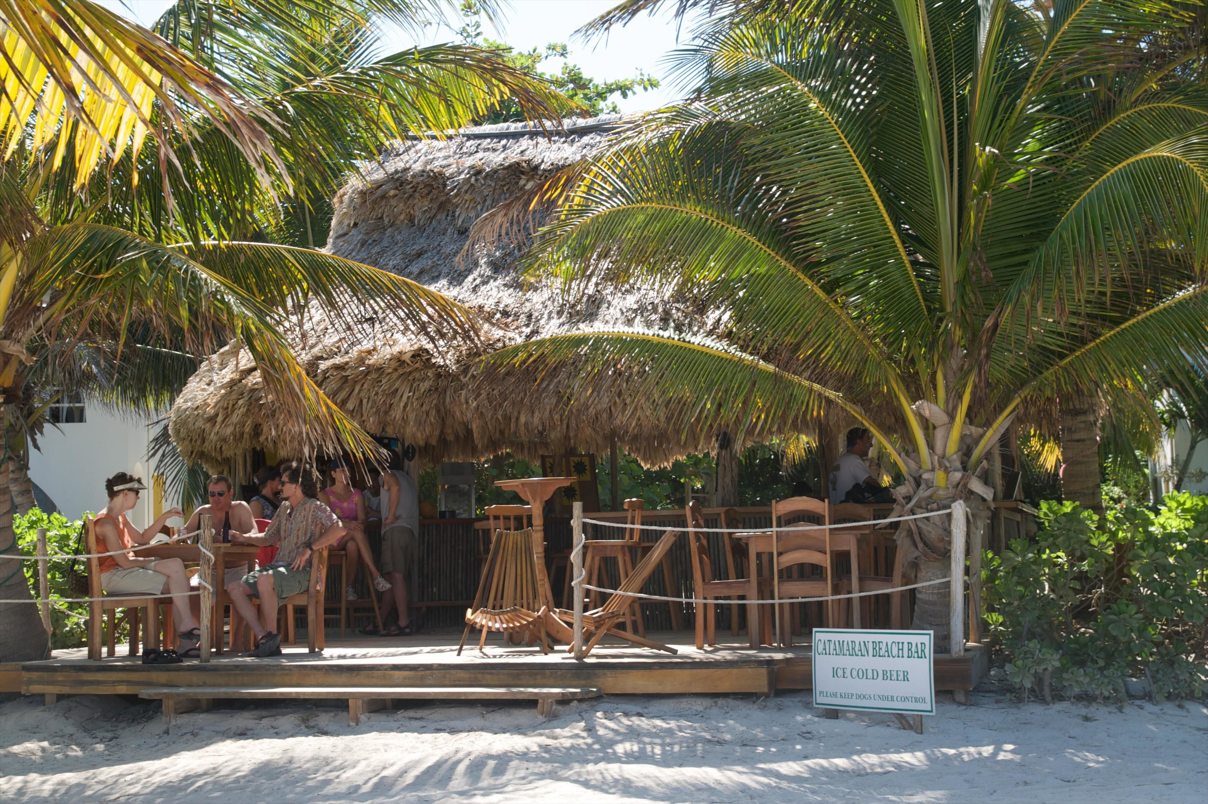 A beach bar with a thatched roof, wooden furniture, and a sign advertising ice cold beer.