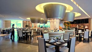 A modern dining area with round tables, high ceilings, and decorative lighting fixtures. - Guoman Hotel Shanghai (Shanghai)