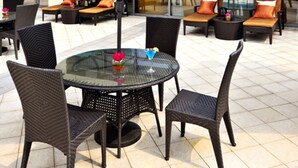 An outdoor seating area with round tables and chairs, green umbrellas, and a view of a modern building in the background. - Guoman Hotel Shanghai (Shanghai)