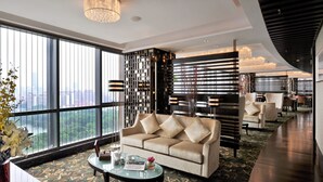 A modern living room with a large window, a sofa, a coffee table, and a decorative wall. - Guoman Hotel Shanghai (Shanghai)