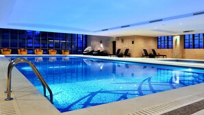 A modern indoor swimming pool with clear blue water, surrounded by lounge chairs and a brick wall. - Guoman Hotel Shanghai (Shanghai)