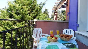 A balcony with a table set for breakfast, including fruits, croissants, and orange juice.