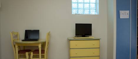A room with a bed, a desk with a laptop, a dresser, a window, and a blue door.