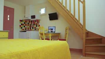 Una camera da letto con un letto, una scrivania con un computer, una sedia, una scala in legno e un angolo cottura con microonde e frigorifero.